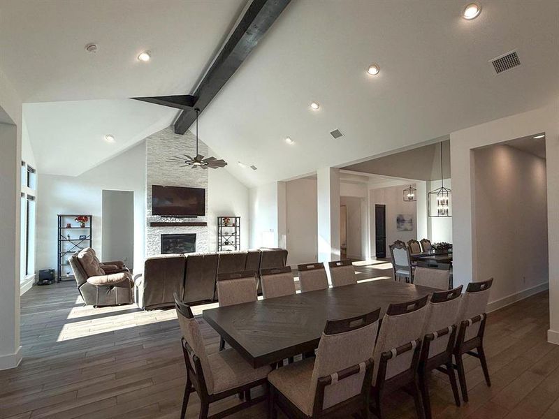 Dining room featuring beamed ceiling, dark wood finished floors, a stone fireplace, a ceiling fan, and recessed lighting Dining room featuring beamed ceiling, dark wood finished floors, a stone fireplace, a ceiling fan, and recessed lighting