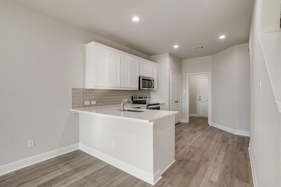 Kitchen featuring a peninsula, stainless steel appliances, recessed lighting, white cabinetry, and light wood finished floors Kitchen featuring a peninsula, stainless steel appliances, recessed lighting, white cabinetry, and light wood finished floors