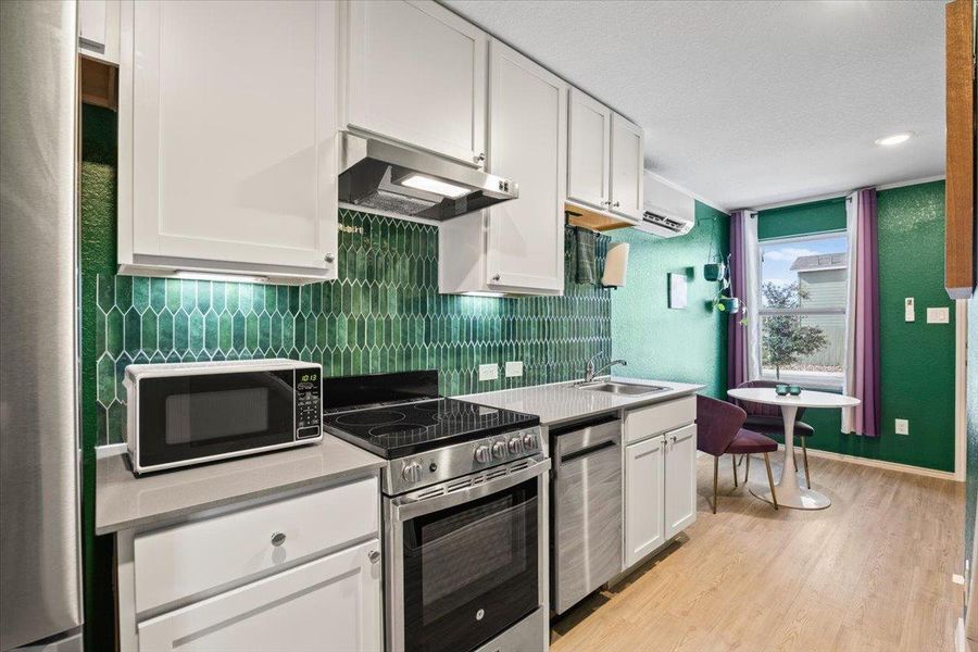 Kitchen featuring stainless steel appliances, white cabinets, light countertops, light wood-style flooring, and decorative backsplash Kitchen featuring stainless steel appliances, white cabinets, light countertops, light wood-style flooring, and decorative backsplash
