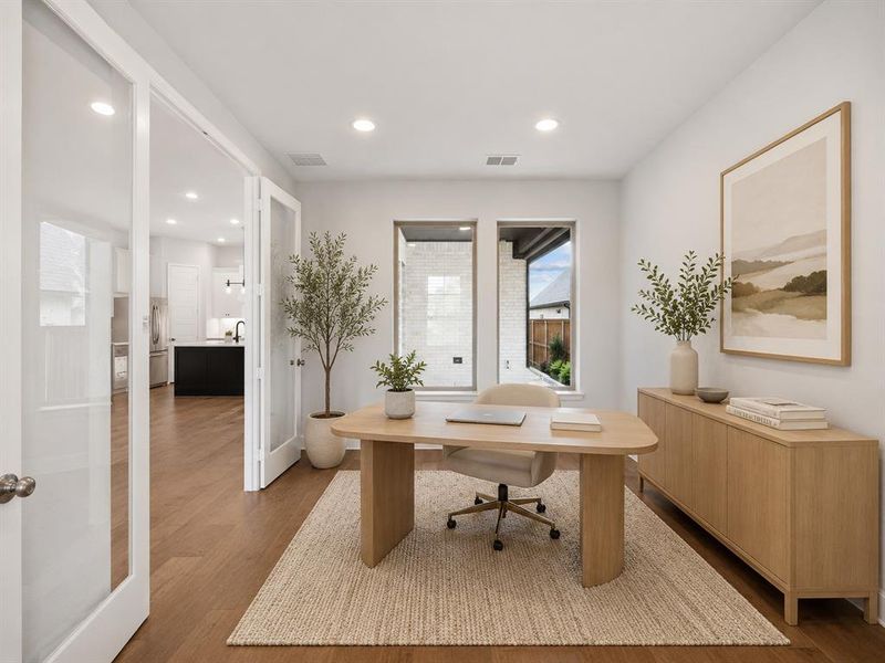 French doors with clear glass panels open to a room featuring two tall windows, recessed ceiling lighting, and wood-finish flooring