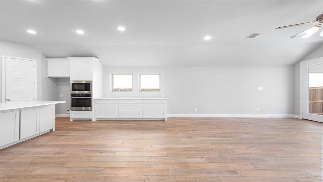 Kitchen with white cabinetry, light hardwood / wood-style flooring, stainless steel oven, black microwave, and ceiling fan