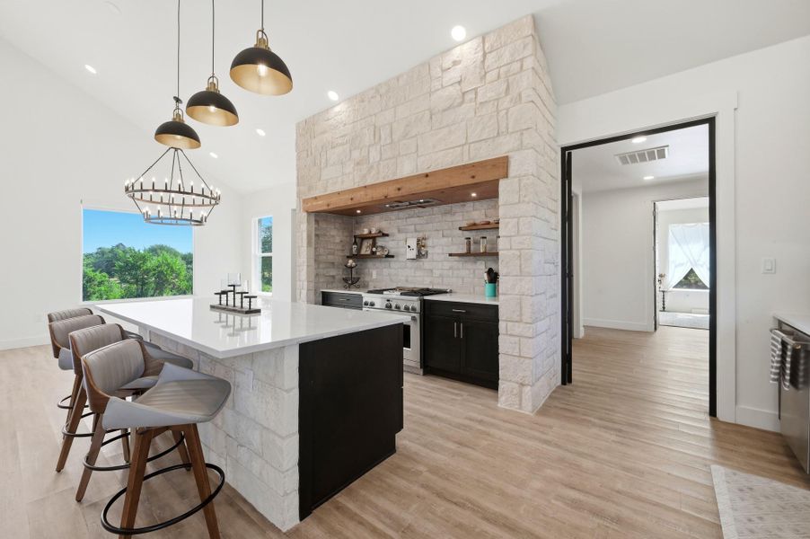 An open kitchen showcases textured stone accents and warm wood-toned flooring beneath high ceilings.