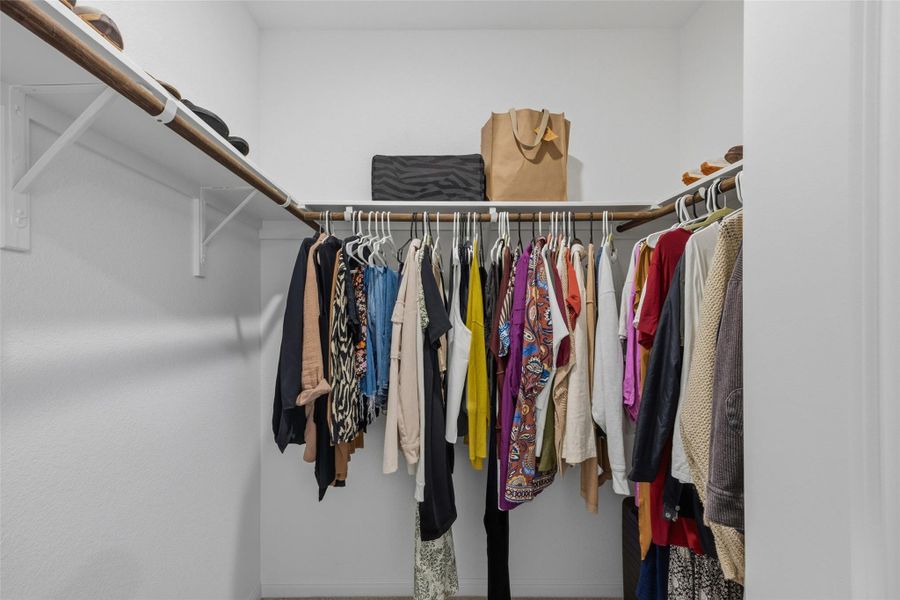 Walk-in closet with white walls, upper shelving, and ample hanging rod space