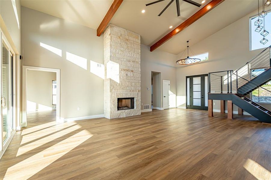 Unfurnished living room featuring high vaulted ceiling, light wood-style flooring, a stone fireplace, beamed ceiling, and stairway Unfurnished living room featuring high vaulted ceiling, light wood-style flooring, a stone fireplace, beamed ceiling, and stairway