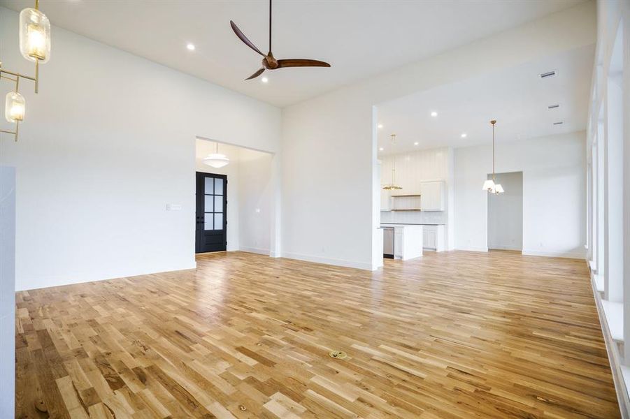 Unfurnished living room with ceiling fan, light hardwood / wood-style floors, and a high ceiling