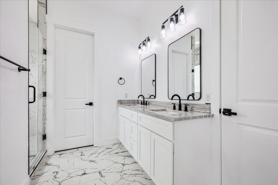 This secondary bathroom includes dual vanities, a walk-in shower and thoughtful finishes, creating a bright, practical, and stylish space.