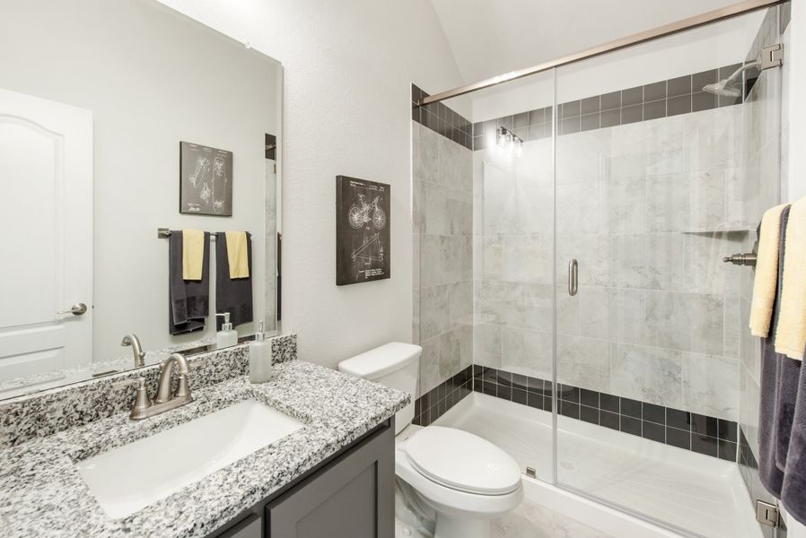 Bathroom with granite vanity, glass-enclosed tub-shower combo, and dark tile accents