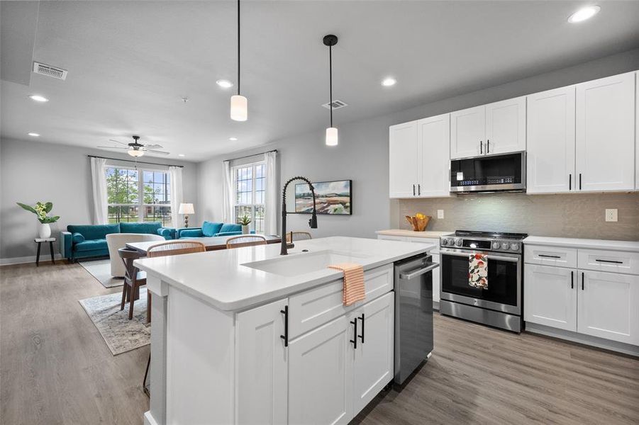 Kitchen featuring white cabinetry, stainless steel appliances, and an island with sink