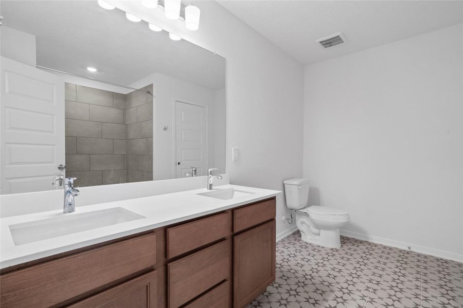This beautifully updated primary bathroom is move-in ready! It showcases stained cabinetry paired with light countertops, dual vanity sinks, a large mirror, Memoir ceramic tile flooring in Gosmo Grey, high ceilings, custom paint, and stylish modern finishes throughout.