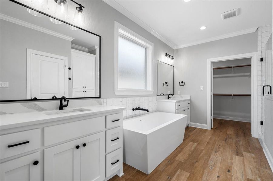 Full bathroom featuring crown molding, light wood finished floors, two vanities, a soaking tub, and a spacious closet Full bathroom featuring crown molding, light wood finished floors, two vanities, a soaking tub, and a spacious closet
