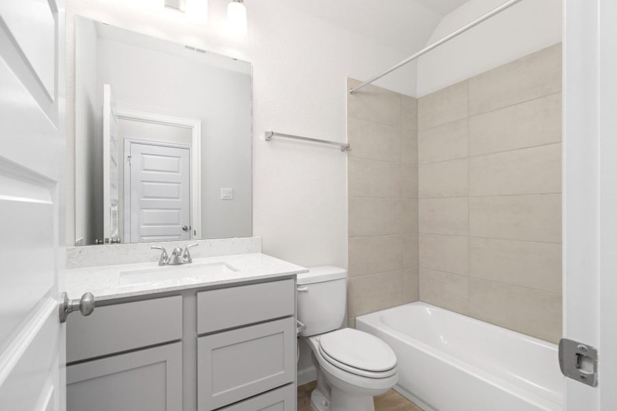 Secondary full bathroom with modern vanity, quartz-style countertop and tiled tub/shower surround.