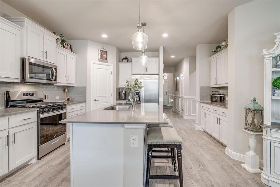 Kitchen featuring a kitchen island with sink, light wood-style flooring, stainless steel appliances, a sink, and white cabinetry