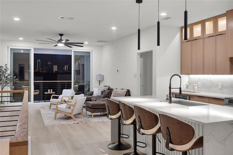 Kitchen featuring light stone countertops, a kitchen breakfast bar, an island with sink, glass insert cabinets, and a ceiling fan