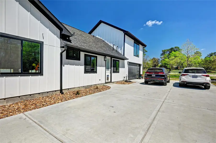 This modern home features a sleek exterior with a white facade and black accents. It boasts a spacious driveway leading to a two-car garage, set in a peaceful, green environment.