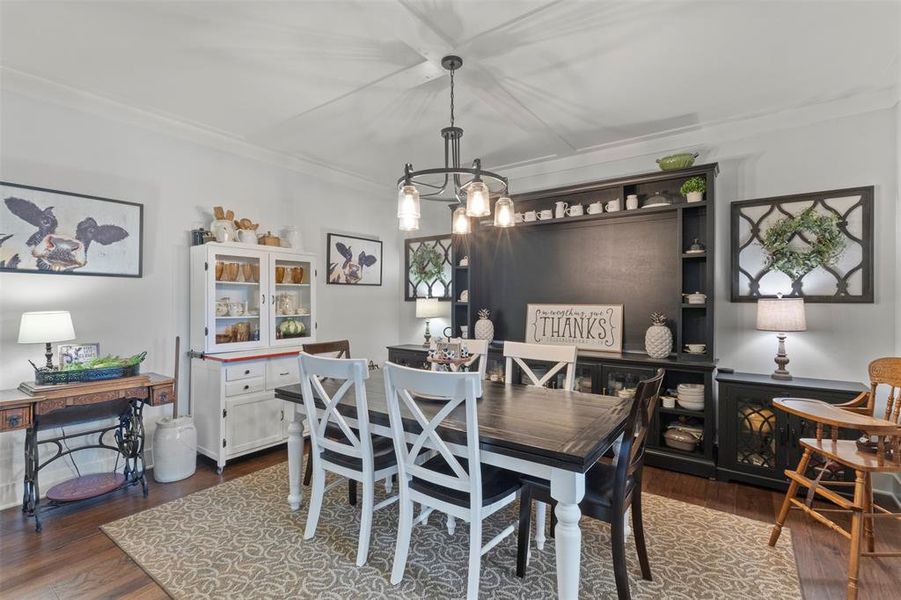 Charming dining area featuring rich wood flooring, tray ceiling detail, statement lighting, built-in display storage, and rustic sliding barn doors that connect beautifully to the kitchen.