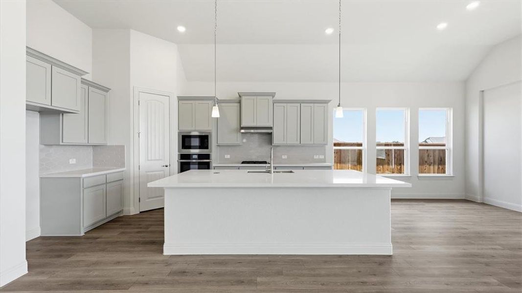 Modern kitchen featuring a large central island with pendant lighting, light gray cabinetry, white countertops, and a full suite of built-in stainless steel appliances