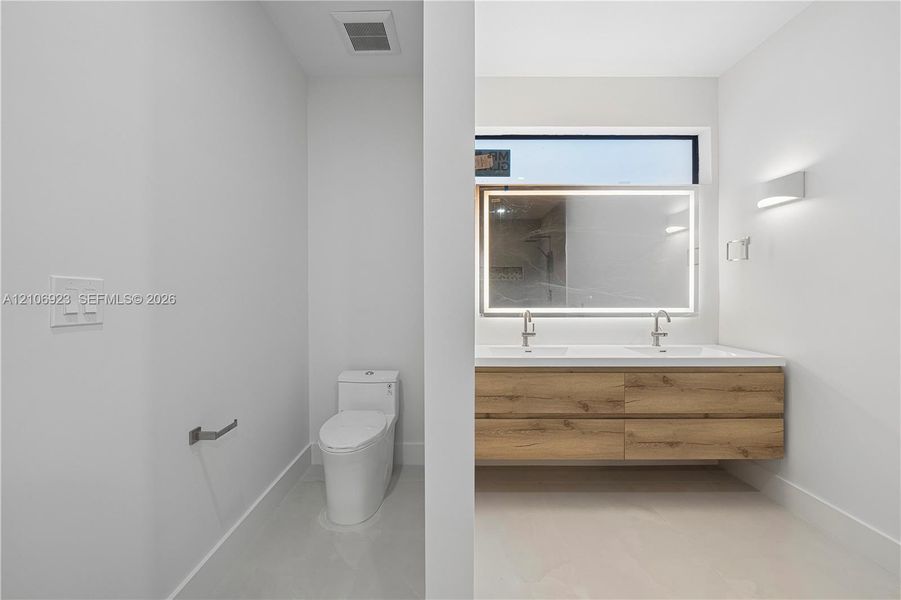 Dual-sink floating vanity with wood-finish cabinetry, rectangular vessel sinks, wall-mounted faucets, and an integrated LED-backlit mirror featuring a horizontal clerestory window Dual-sink floating vanity with wood-finish cabinetry, rectangular vessel sinks, wall-mounted faucets, and an integrated LED-backlit mirror featuring a horizontal clerestory window