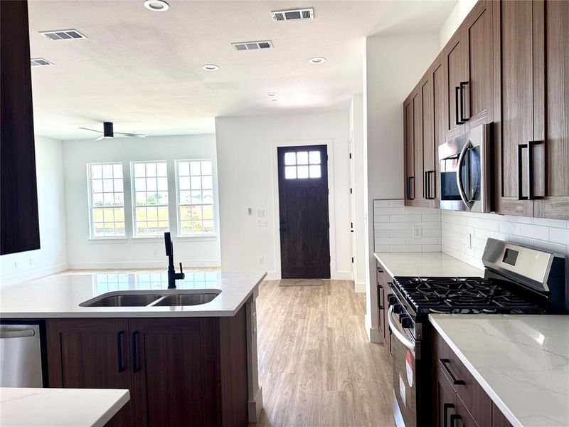Kitchen with stainless steel appliances, light wood-style flooring, recessed lighting, decorative backsplash, and light stone counters