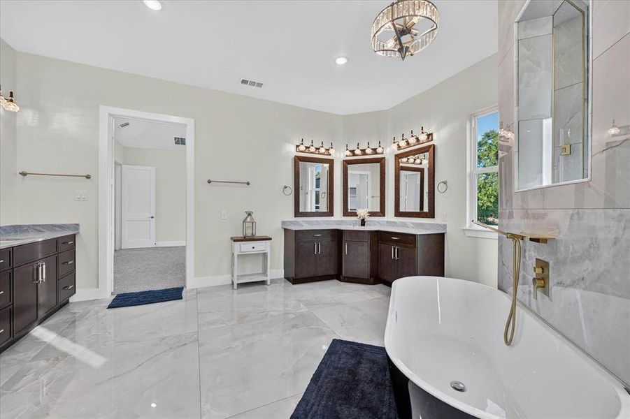 Spacious bathroom featuring a freestanding soaking tub, large format tile flooring, and a dual vanity with dark wood cabinetry and stone countertops Spacious bathroom featuring a freestanding soaking tub, large format tile flooring, and a dual vanity with dark wood cabinetry and stone countertops