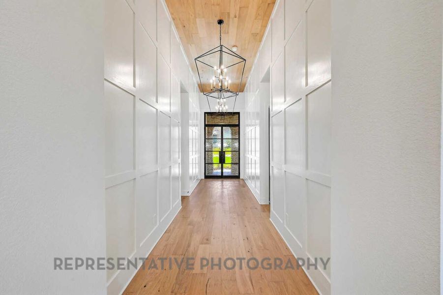 Hallway with a decorative wall, light wood finished floors, a chandelier, and wooden ceiling Hallway with a decorative wall, light wood finished floors, a chandelier, and wooden ceiling