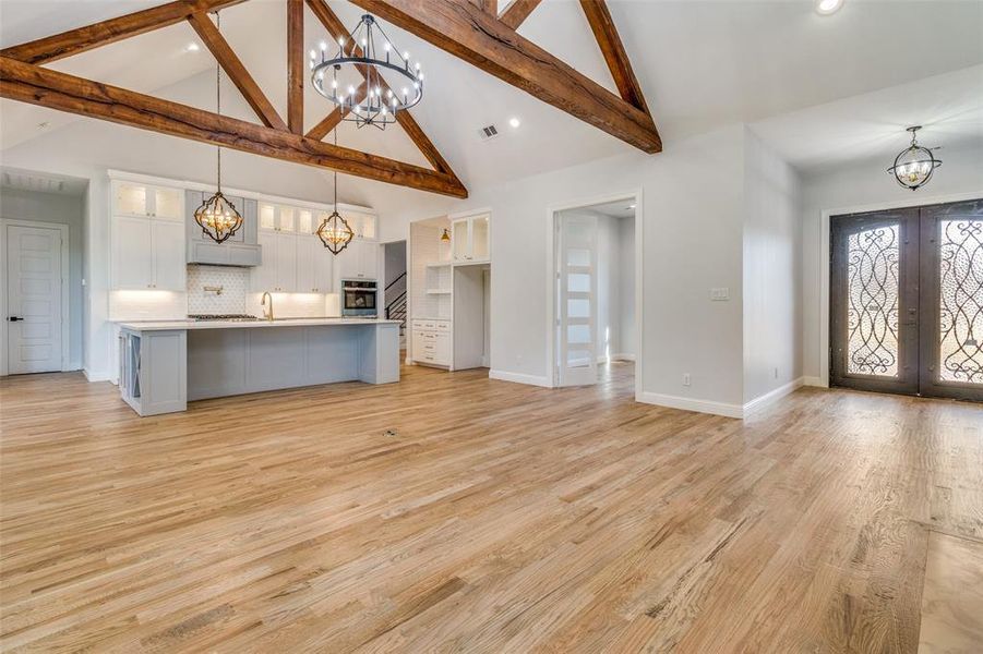 Unfurnished living room with high vaulted ceiling, light wood-type flooring, beamed ceiling, sink, and french doors