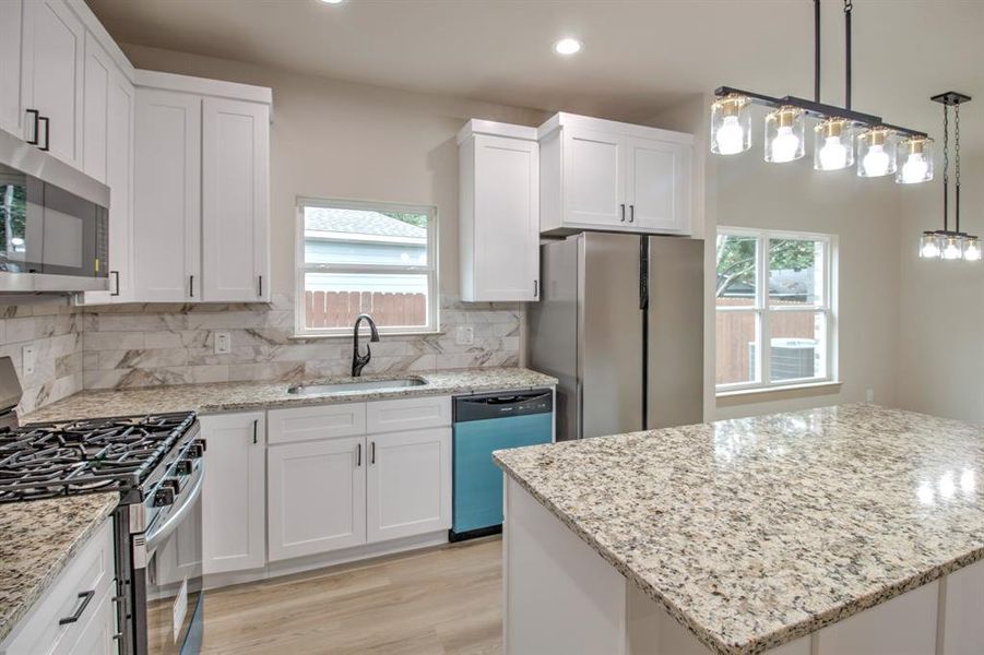 Kitchen with stainless steel appliances, tasteful backsplash, light stone countertops, a center island, and white cabinets