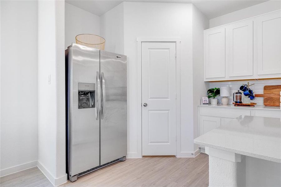 Kitchen featuring light wood-type flooring, stainless steel refrigerator with ice dispenser, white cabinetry, and baseboards