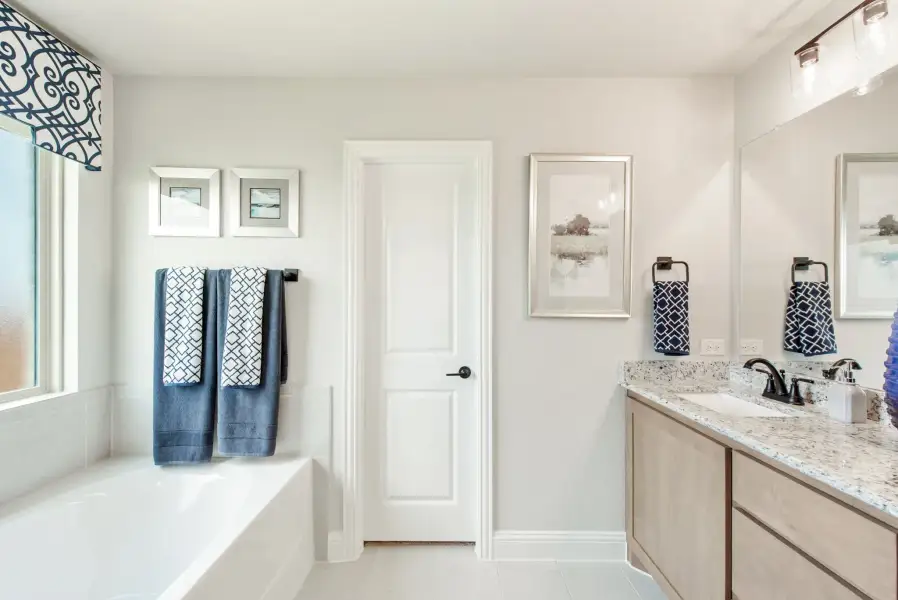 Bathroom with soaking tub, granite vanity, wood cabinets, and large mirror with blue accent towels