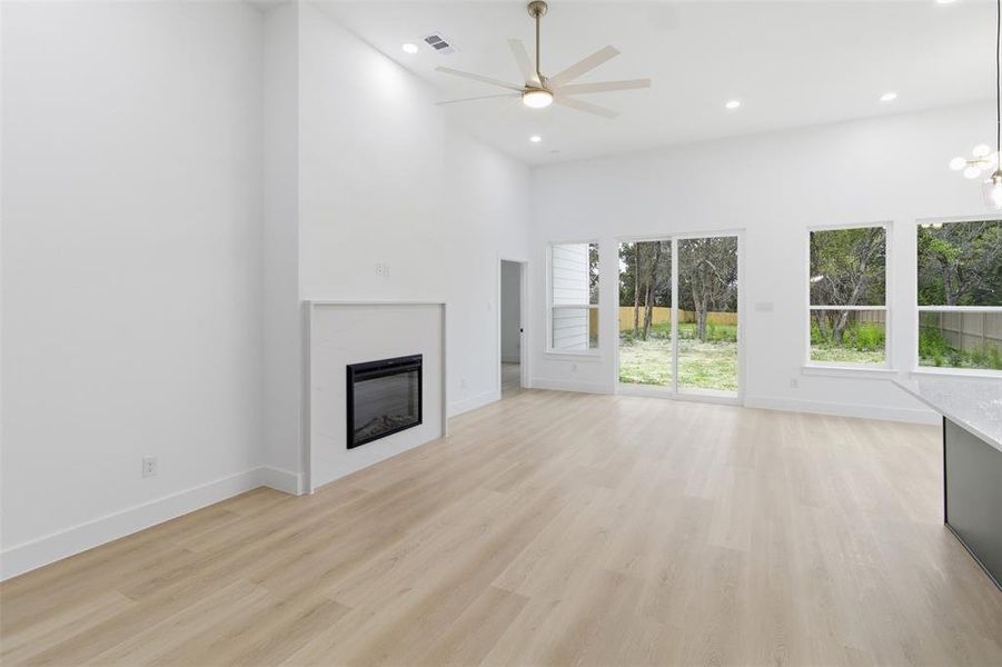 Unfurnished living room featuring a glass covered fireplace, light wood-style flooring, a high ceiling, recessed lighting, and a ceiling fan