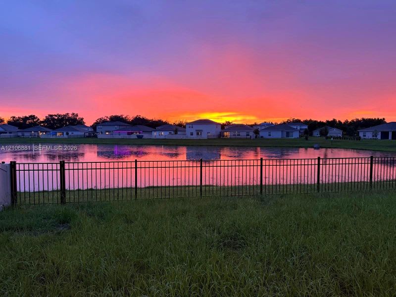 Waterfront property featuring a metal perimeter fence and sunset backdrop