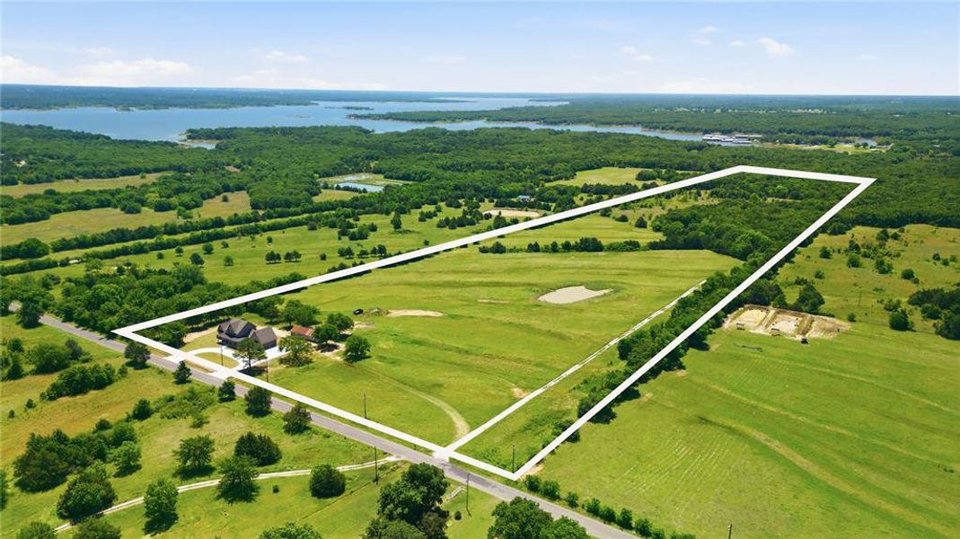 Expansive green acreage featuring a main residence, a private pond, and scattered mature trees
