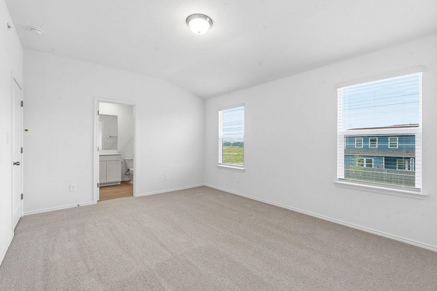 Spacious room featuring carpeting, two windows with blinds, a ceiling-mounted light fixture, and a doorway to a private bathroom with a vanity and toilet Spacious room featuring carpeting, two windows with blinds, a ceiling-mounted light fixture, and a doorway to a private bathroom with a vanity and toilet
