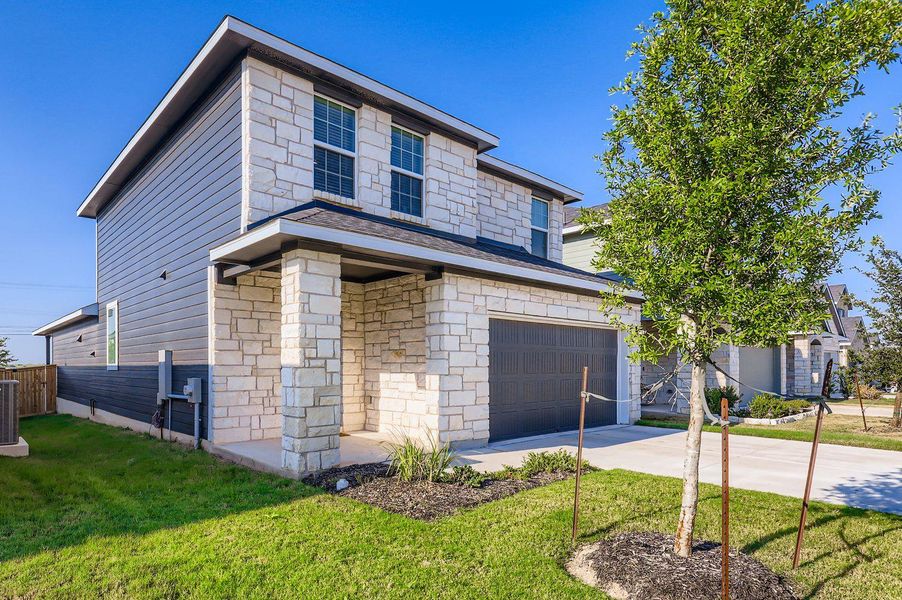 View of front of property with stone siding, an attached garage, driveway, and a front lawn