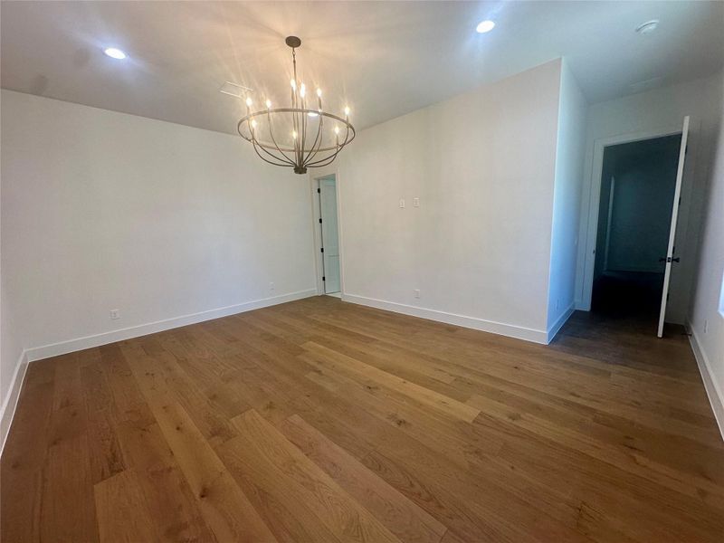 Rich hardwood flooring pairs with a classic iron chandelier and recessed lighting in this versatile space.