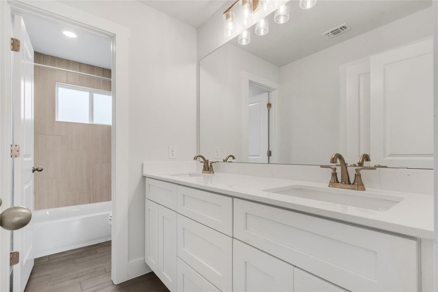 Double vanity in this primary bathroom offers ample counter space and storage, complemented by a contemporary tub-shower combo.