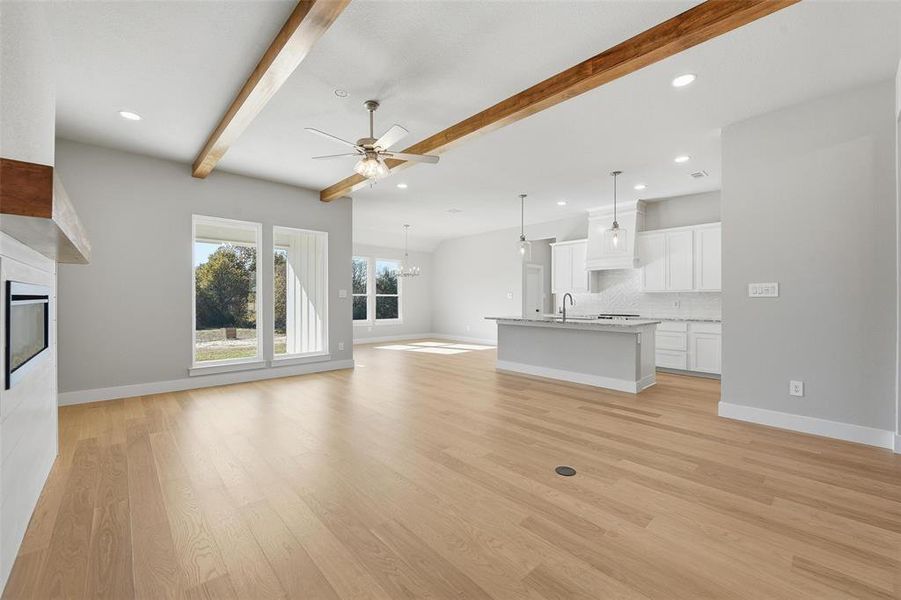 Unfurnished living room with a glass covered fireplace, beamed ceiling, a chandelier, a ceiling fan, and light wood-style floors Unfurnished living room with a glass covered fireplace, beamed ceiling, a chandelier, a ceiling fan, and light wood-style floors
