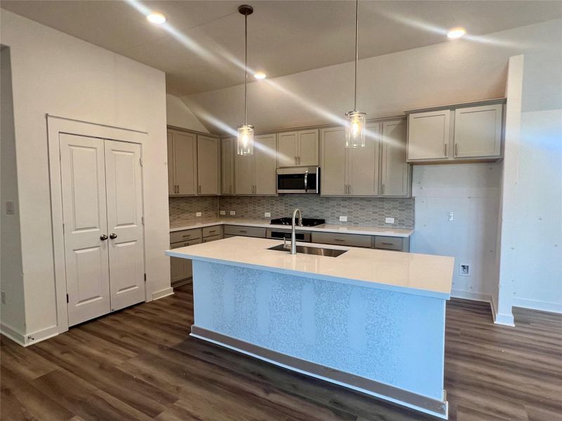 Kitchen featuring stainless steel microwave, gray cabinetry, vaulted ceiling, tasteful backsplash, and dark wood-style floors