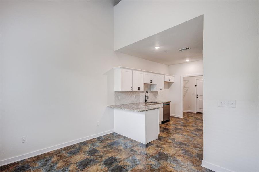 Kitchen with white cabinets, kitchen peninsula, dark tile patterned flooring, decorative backsplash, and dishwasher