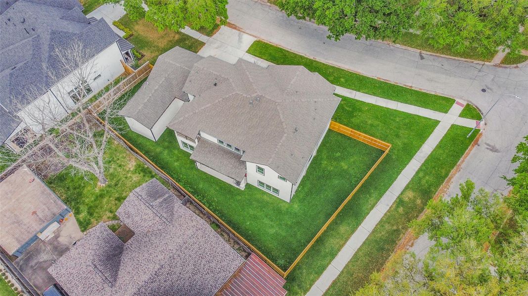 This aerial view showcases a spacious two-story home on a corner lot with a well-maintained lawn and fenced backyard, offering privacy and ample outdoor space. The surrounding neighborhood appears quiet and lined with trees.