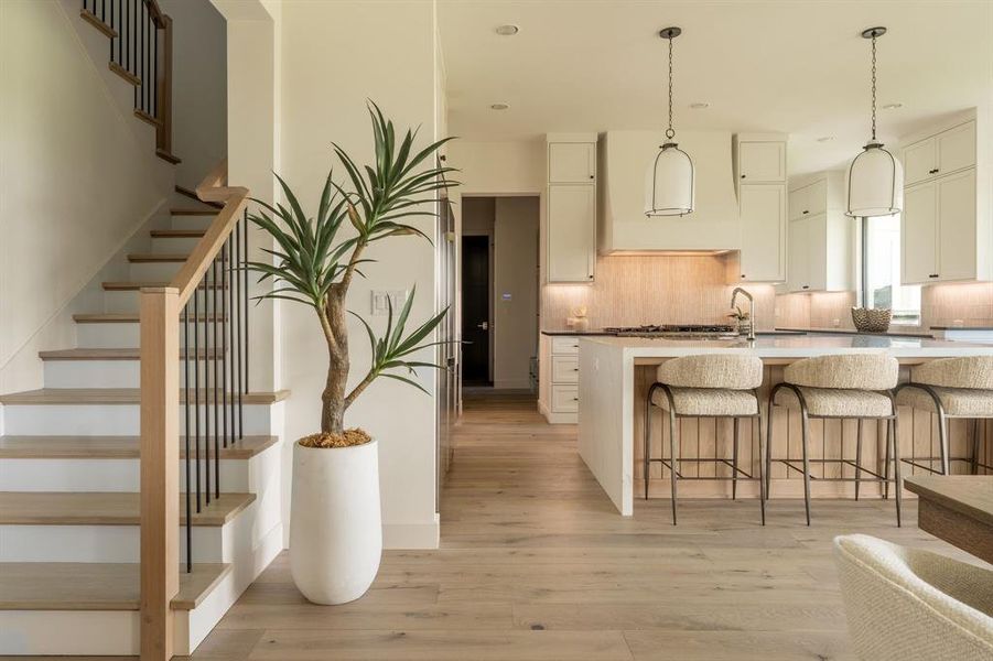 Kitchen with a kitchen breakfast bar, light wood-style flooring, range hood, decorative backsplash, and a kitchen island with sink Kitchen with a kitchen breakfast bar, light wood-style flooring, range hood, decorative backsplash, and a kitchen island with sink