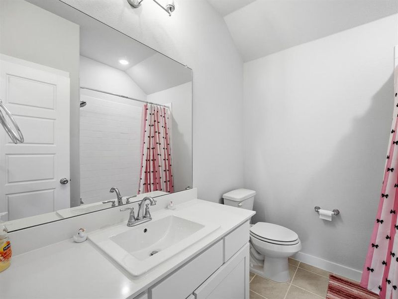 Bathroom featuring light tile patterned flooring, vanity, curtained shower, and vaulted ceiling