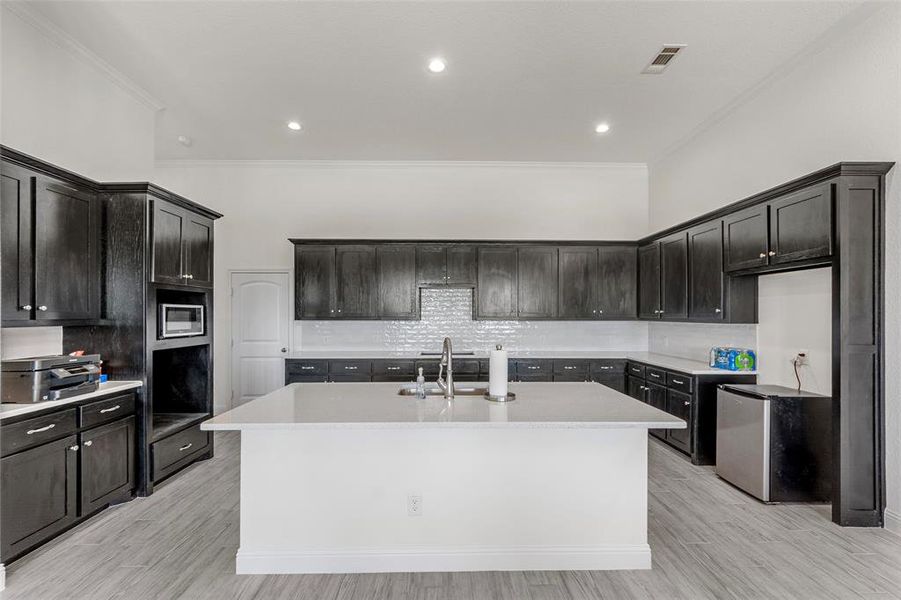 Kitchen with crown molding, a sink, freestanding refrigerator, decorative backsplash, and a center island with sink