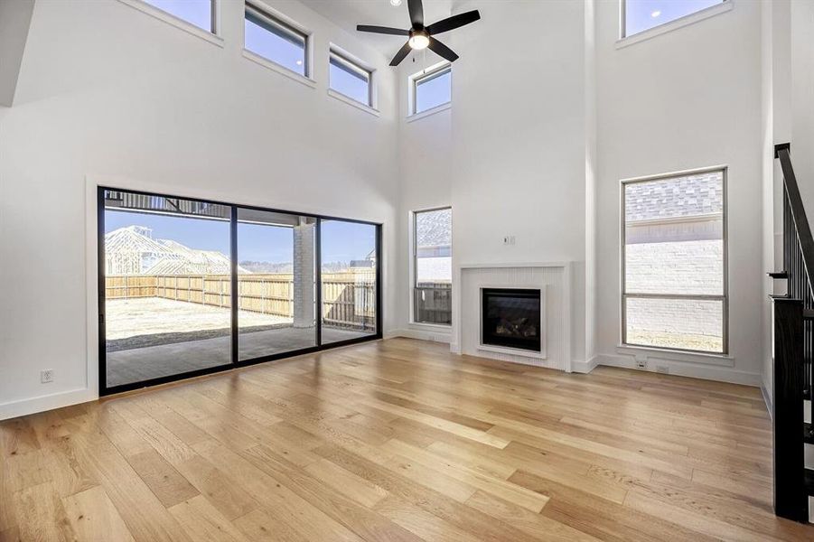 Unfurnished living room with ceiling fan, a glass covered fireplace, light wood finished floors, and a high ceiling