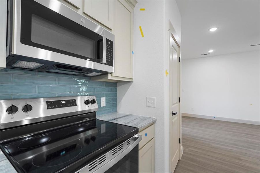 Kitchen featuring baseboards, light wood finished floors, stainless steel appliances, white cabinets, and backsplash