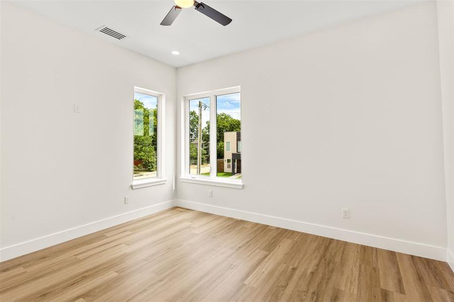 Light-filled room featuring wood-finish flooring, two large windows, a ceiling fan with integrated lighting, recessed ceiling lighting, and crisp white walls