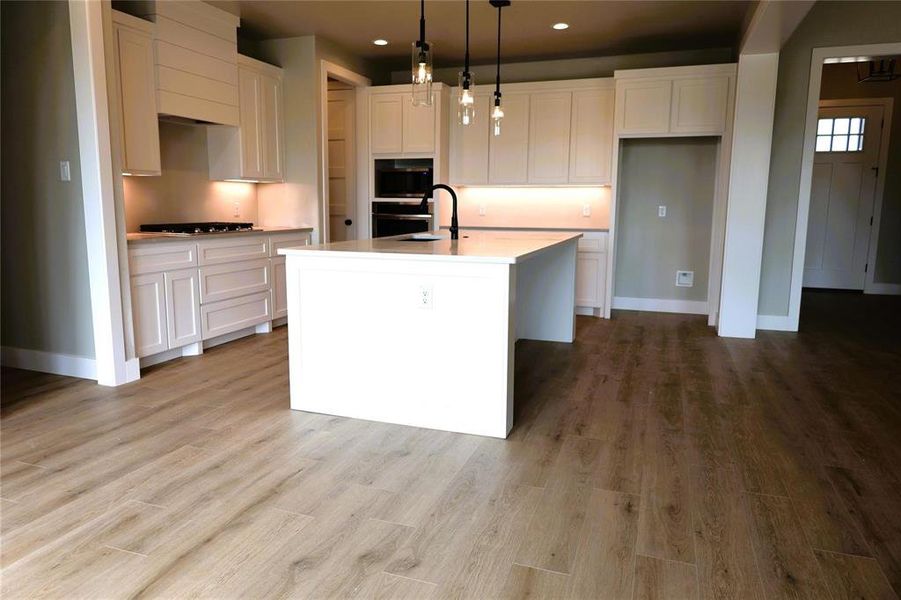 Kitchen with white cabinets, a center island with sink, and light wood-type flooring