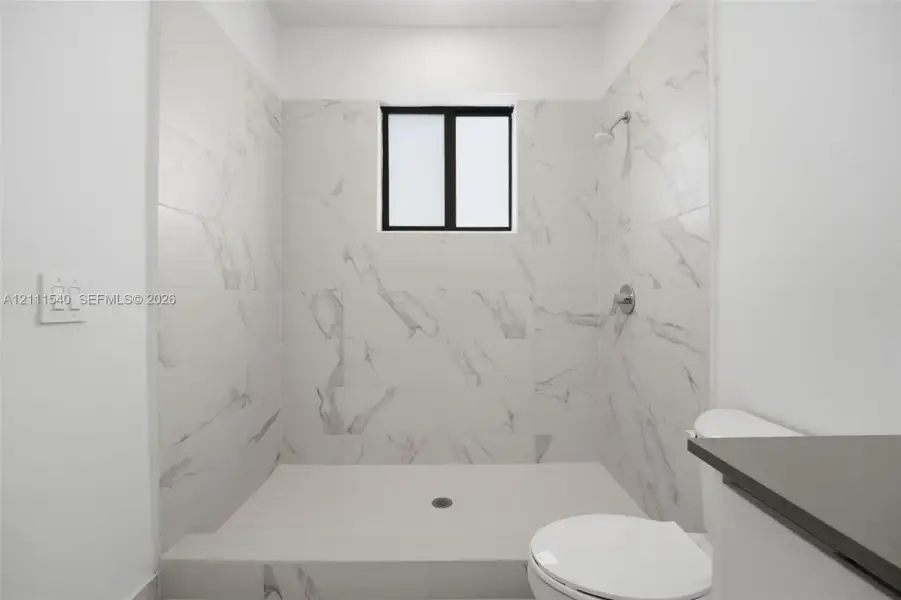 Walk-in shower featuring floor-to-ceiling stone-finish tile surround, a built-in shower head, and a privacy window
