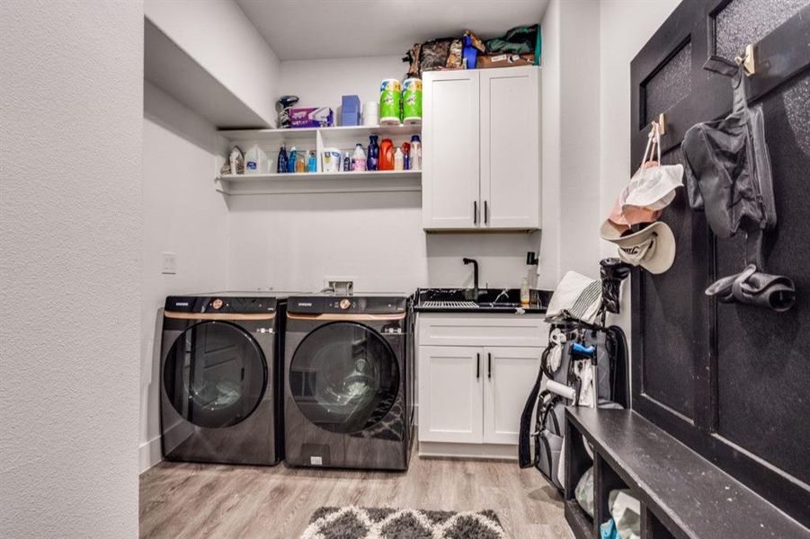 Laundry room with washing machine and dryer, light wood-type flooring, and cabinet space