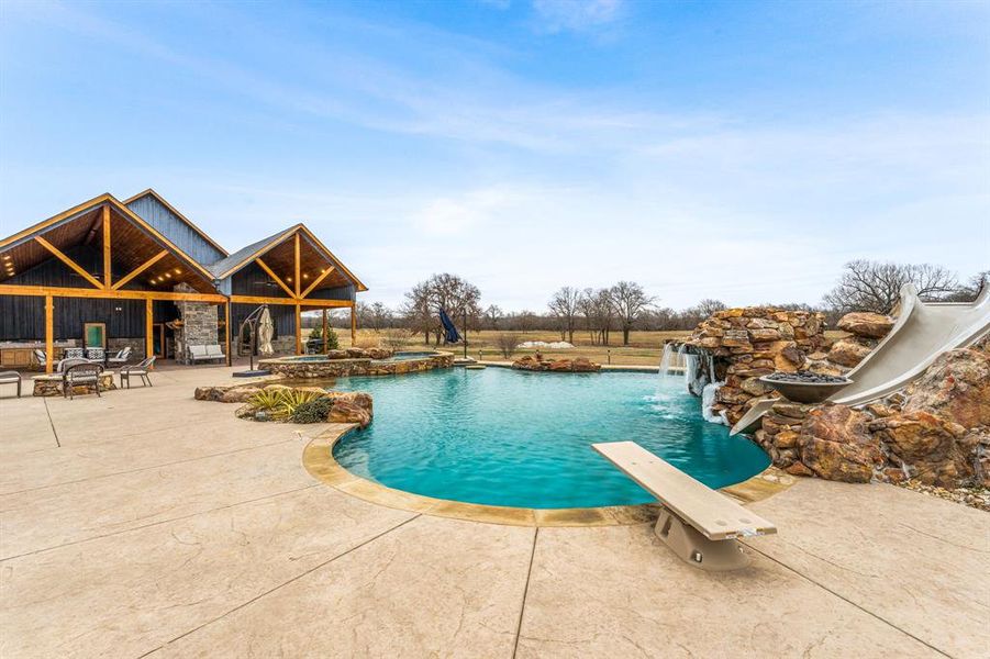 View of pool with a patio area, a diving board, a water slide, and a pool with connected hot tub