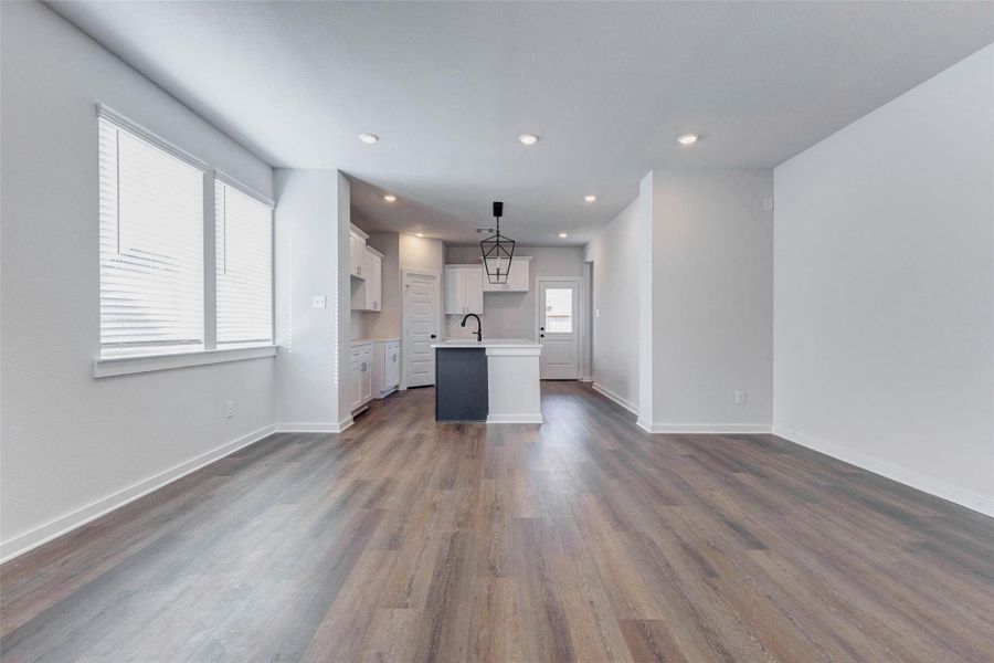 Spacious and inviting, this open-concept living area blends seamlessly with the kitchen for effortless entertaining. Recessed lights and wide windows create a bright, airy atmosphere, while the continuous luxury vinyl plank flooring offers warmth and durability throughout.